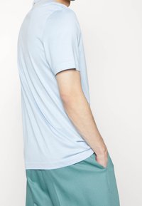 Světle modré tričko s krátkým rukávem vyrobené z měkké tkaniny, s uvolněným střihem a zakulaceným lemem, v kombinaci s tyrkysovými kalhotami s bočními kapsami.