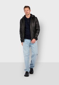 Sort læderjakke med hætte og lynlås, marineblå polo t-shirt under, lyseblå jeans og sorte sko. Enkelt, afslappet outfit.