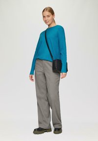 Cyanfarbener, gerippter Pullover mit weiten Ärmeln, kombiniert mit grauen Hosen. Schwarze Umhängetasche mit strukturierter Oberfläche. Klobige schwarze Stiefel runden das Outfit ab.