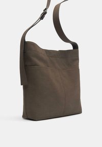 Smeđa platnena torba za rame s mekom teksturom, podešavnim remenom i detaljima šavova. Ima jednostavan, pravokutni dizajn.