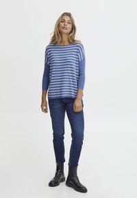Gestreifter blau-weißer Pullover mit Dreiviertelärmeln, kombiniert mit eng anliegenden dunklen Jeans und schwarzen Ankle Boots.