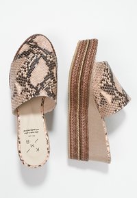 Beige ormskinns slide-sandaler med en bred rem, texturerad yta och en vävd brun plattformssula. Diskreta guldackenter på sulan.