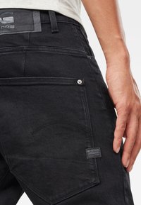 Jeans de mezclilla negra con un parche de cuero, detalles de costura sutil en los bolsillos y un acabado texturizado.