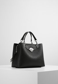Bolso de mano de cuero negro con diseño estructurado, herrajes plateados, dos asas cortas y un bolsillo lateral con cremallera. Cuenta con un detalle de logo.