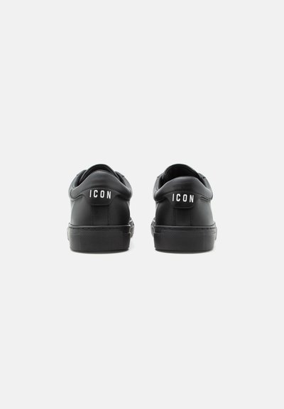 Paire de baskets noires basses vues de dos, chacune avec le mot « ICON » imprimé en blanc sur la languette du talon.