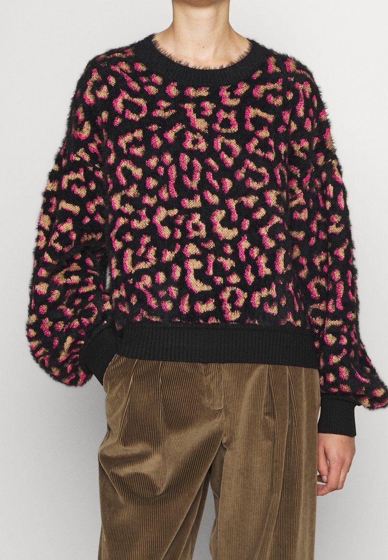 Svart, fluffig tröja med djärv rosa och tan leopardtryck; ribbade svarta manschetter och nederkant; avslappnad, överdimensionerad passform. Matchad med bruna kordflorsbyxor.
