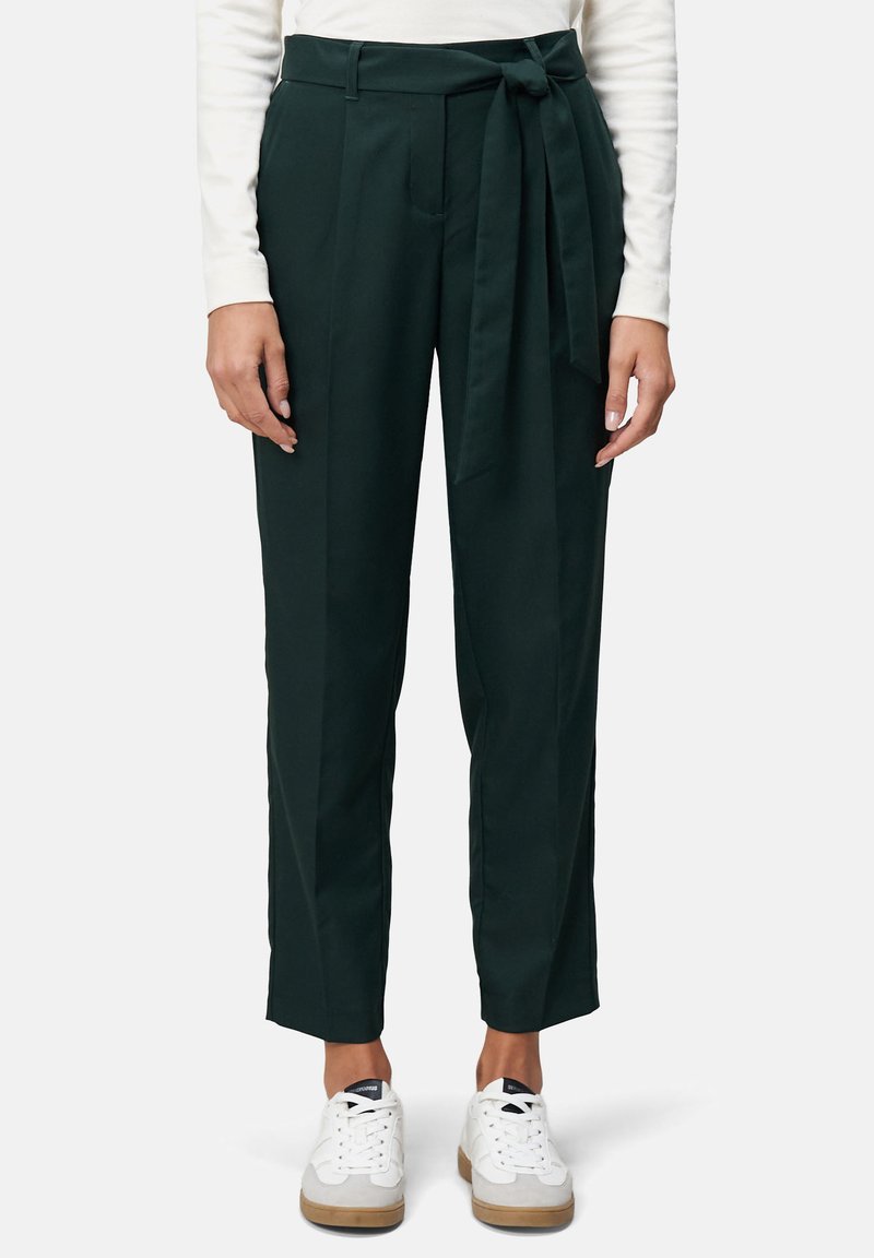 Donkergroene op maat gemaakte broek met een strikceintuur, voorzien van een rechte snit en zijzakken; gedragen met witte sneakers. Glad stoftextuur.