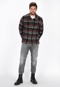 Svart, röd och grå rutigt flanellskjorta med knäppning framtill, som bärs över en vit t-shirt. Matchas med grå jeans och svarta snörkängor.