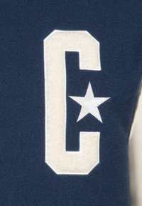 Felpa navy con una grande lettera "C" in feltro crema e una stella bianca ricamata sul davanti, con una texture morbida e bordi arrotondati.