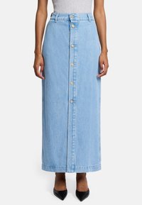 Lichtblauwe denim maxi rok, high-waisted, met een sluiting aan de voorkant met zeven gouden knopen, gestikte zoom, rechte snit, gecombineerd met zwarte hakken.