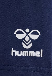 Mörkblått tyg med en vit logotyp av två symmetriska kurvor ovanför ett chevronmönster och ordet "hummel" i feta, rundade bokstäver.