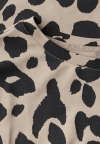 Leopard print fabric featuring large black spots on a light beige background, with a round neckline and visible stitching details.