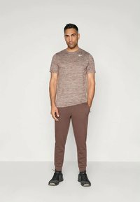 Conjunto atlético que presenta una camiseta corta marrón texturizada y pantalones marrones ajustados, complementados con zapatillas de correr negras.