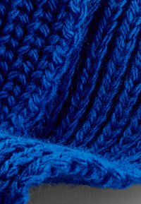 Tela gruesa de punto en azul profundo, con relieve texturizado y patrones trenzados, que muestra una textura suave y peluda y un tono vibrante.