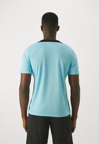 Camiseta deportiva azul claro con un collar negro. Mangas cortas, tejido texturado, diseño ajustado con un color sólido y sin logotipos ni patrones visibles.