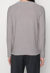 Top z długim rękawem w jasnoszarym kolorze wykonany z miękkiego materiału. Posiada okrągły dekolt i delikatne przeszycia wzdłuż krawędzi. Prosty, minimalistyczny design.