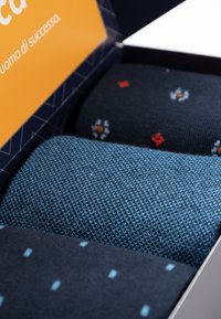 Tre rotoli di calze in una scatola: uno blu scuro uniforme, uno blu navy strutturato con pois blu chiaro, uno blu scuro con motivi floreali.