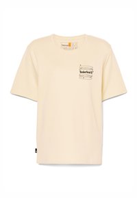 Camiseta de manga corta color crema hecha de algodón, con un estampado del logo negro de Timberland en el pecho y una etiqueta lateral.