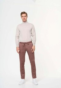 Suéter de cuello alto gris claro combinado con pantalones marrón rojizo que presentan una cintura con cordón, tejido texturizado y zapatillas blancas.