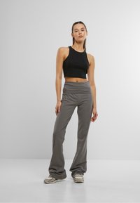 Top corto nero e pantaloni flare grigi, in tessuto morbido, vita alta e elastico in vita. Sneakers grigie con motivo tenue e dettagli.