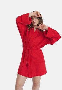 Czerwona lniana szlafrok z szerokimi rękawami i paskiem. Tkanina wydaje się teksturowana, a szlafrok ma długość powyżej kolana i luźny fason.