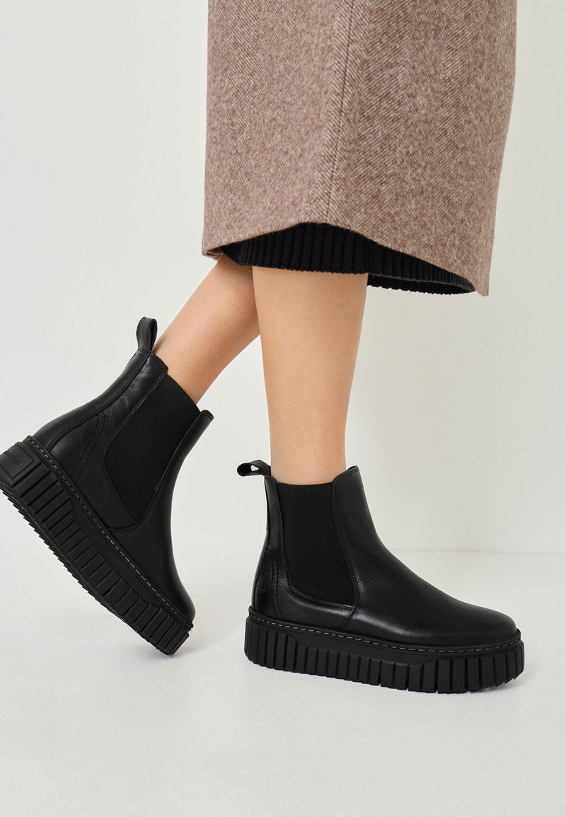 Svarta läder Chelsea-boots med elastiska sidopaneler, tjock ribbad sula och dragflikar bak; slät yta och stilren design.
