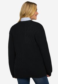 Cardigan nero a maglia con vari motivi testurizzati, incluso un design a zigzag. Vestibilità ampia con maniche lunghe e orlo dritto.