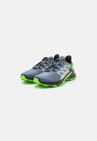 Chaussures de trail running avec un upper gris, des accents noirs et une semelle extérieure vert fluo. Conçues pour la durabilité avec une finition texturée et un embout renforcé.