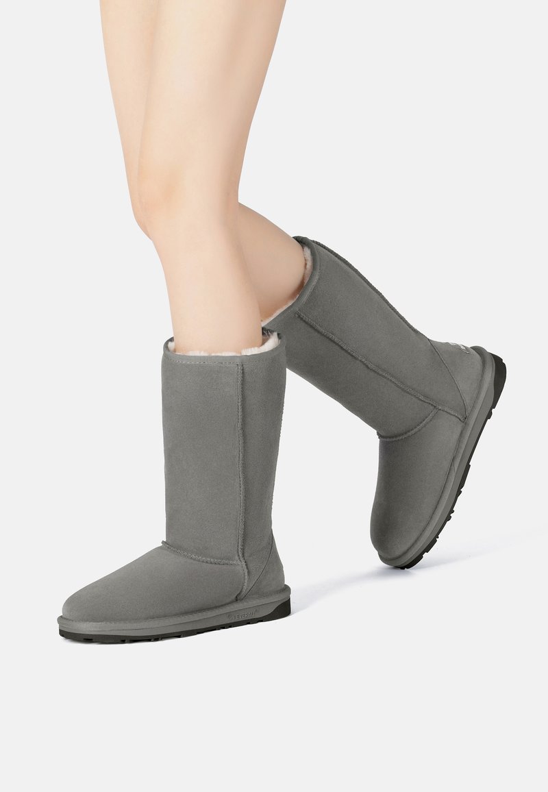 Graue lange Stiefel aus Wildleder mit einem weichen Futter aus Fell, runder Zehe, flacher Sohle und Nahtdetails entlang der Nähte.
