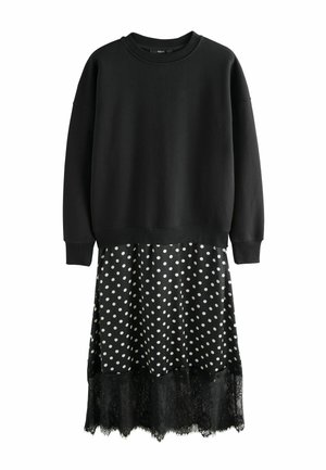 Schwarzer Sweatshirt-Oberteil mit lockerem Schnitt, kombiniert mit einem schwarzen gepunkteten Kleid mit Spitzenrand, das weiche Texturen und kontrastierende Muster verbindet.