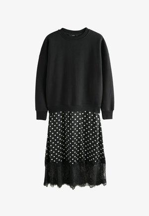 Czarna bluza o luźnym kroju, zestawiona z czarną sukienką w groszki z koronkowym wykończeniem, łącząca miękkie tekstury i kontrastujące wzory.