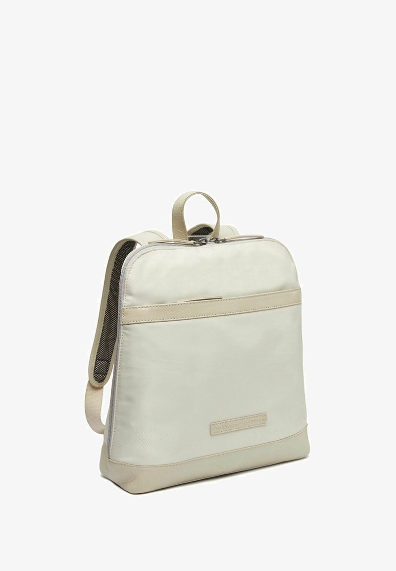Mochila beige con un acabado de tela suave, detalles de cuero blando, un asa en la parte superior y correas ajustables, que cuenta con un compartimento principal con cremallera.