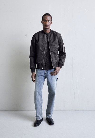 Sort bomberjakke med lynlås, parret med en sort t-shirt, lyseblå lige jeans og sorte sko. Glat materiale, ingen mønstre.