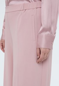 Rosa satinbluse med en glat tekstur. Har en afslappet pasform, lange ærmer og en knapdetalje ved manchetterne. Skræddersyet for komfort.