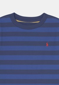 Niebieski t-shirt w paski z naprzemiennymi ciemnoniebieskimi i jasnoniebieskimi pasami, okrągłym dekoltem oraz małym czerwonym logo na lewej piersi.