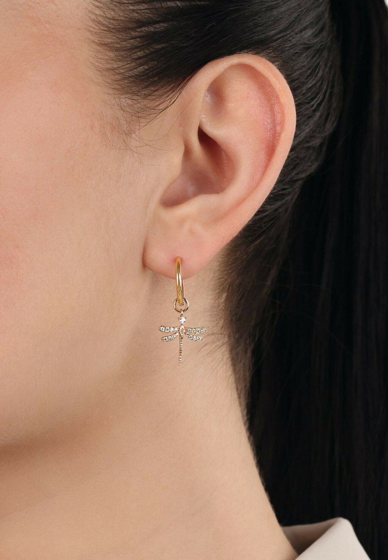 Pendiente de aro dorado con un diseño de libélula adornado con piedras de rhinestone transparentes. El pendiente cuelga debajo del lóbulo de la oreja, mostrando detalles intrincados.