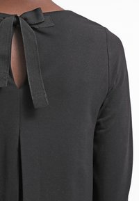 Svart långärmad topp med en nyckelhålsöppning i ryggen och detaljer med satinband. Slät tygstruktur med en figurnära siluett.