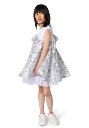 Robe en sequins argentés avec volants superposés, haut en coton blanc et sous-couche en tulle. Associée à des baskets blanches.