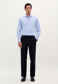 Lichtblauw gestreept shirt met een button-down kraag, gecombineerd met donkere marineblauwe broek en zwarte schoenen; eenvoudig design zonder zichtbare patronen.