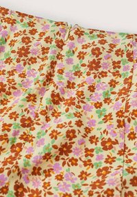 Tissu beige avec un petit motif floral rouge, violet et vert et une fermeture éclair beige à la couture du tissu.