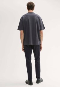 Mörkgrå kortärmad skjorta med avslappnad passform, tillsammans med mörkblå smala byxor och svarta skor, sedd bakifrån.