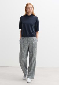 Pullover blu navy con cappuccio, maniche corte e orlo elastico abbinato a pantaloni a palazzo grigi a scacchi e sneakers bianche.