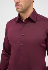 Bordeaux langemouwen shirt met een gladde textuur, spitse kraag en zwarte knopen. Getailleerde pasvorm die een slanke uitstraling benadrukt.