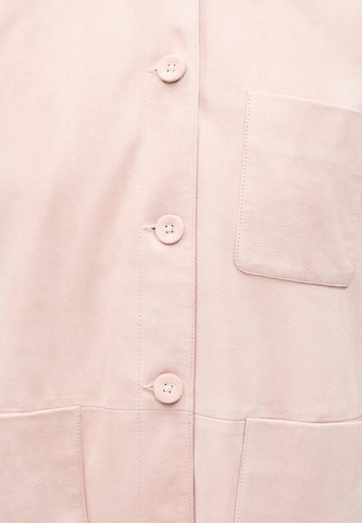 Ανοιχτό ροζ πουκάμισο με τέσσερα στρογγυλά κουμπιά κατά μήκος του κέντρου και μία τσέπη στο στήθος στη δεξιά πλευρά.