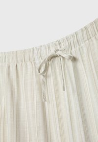 Shorts en tissu beige clair avec des rayures verticales, une taille élastique et un cordon de serrage noué. Le matériau semble doux et texturé.