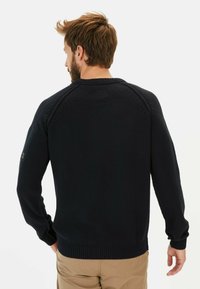 Marineblauer Strickpullover mit geripptem Saum und Bündchen, ausgestattet mit Raglanärmeln und einem kleinen Logo-Patch am linken Ärmel.