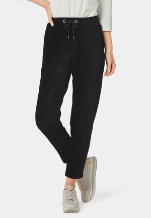 Schwarze, weiche Stoffhosen mit einem Kordelzugbund. Z tapered Design und seitlichen Taschen, kombiniert mit hellen Sneakern mit goldenen Akzenten.