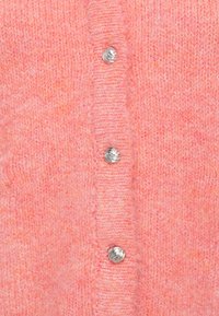 Różowy sweter robiony na drutach o miękkiej strukturze z zapięciem na guziki, metalicznymi srebrnymi guzikami i lekko melanżowym wyglądem.