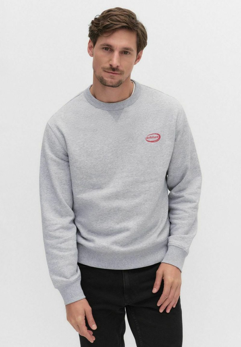 Szara bluza z okrągłym dekoltem, długimi rękawami i małym czerwonym owalnym logo na piersi. Styl jest luźny, wykonana z miękkiego materiału.