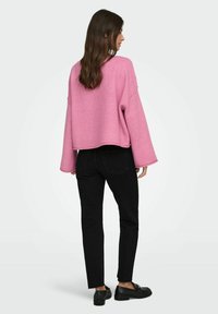 Różowy krótki sweter z luźnymi rękawami, zestawiony z czarnymi dżinsami i czarnymi butami. Miękki materiał i luźny krój. Widok z tyłu.